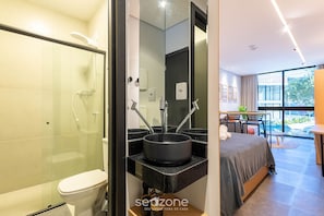 Un baño moderno con ducha de vidrio, lavamanos negro y un inodoro.