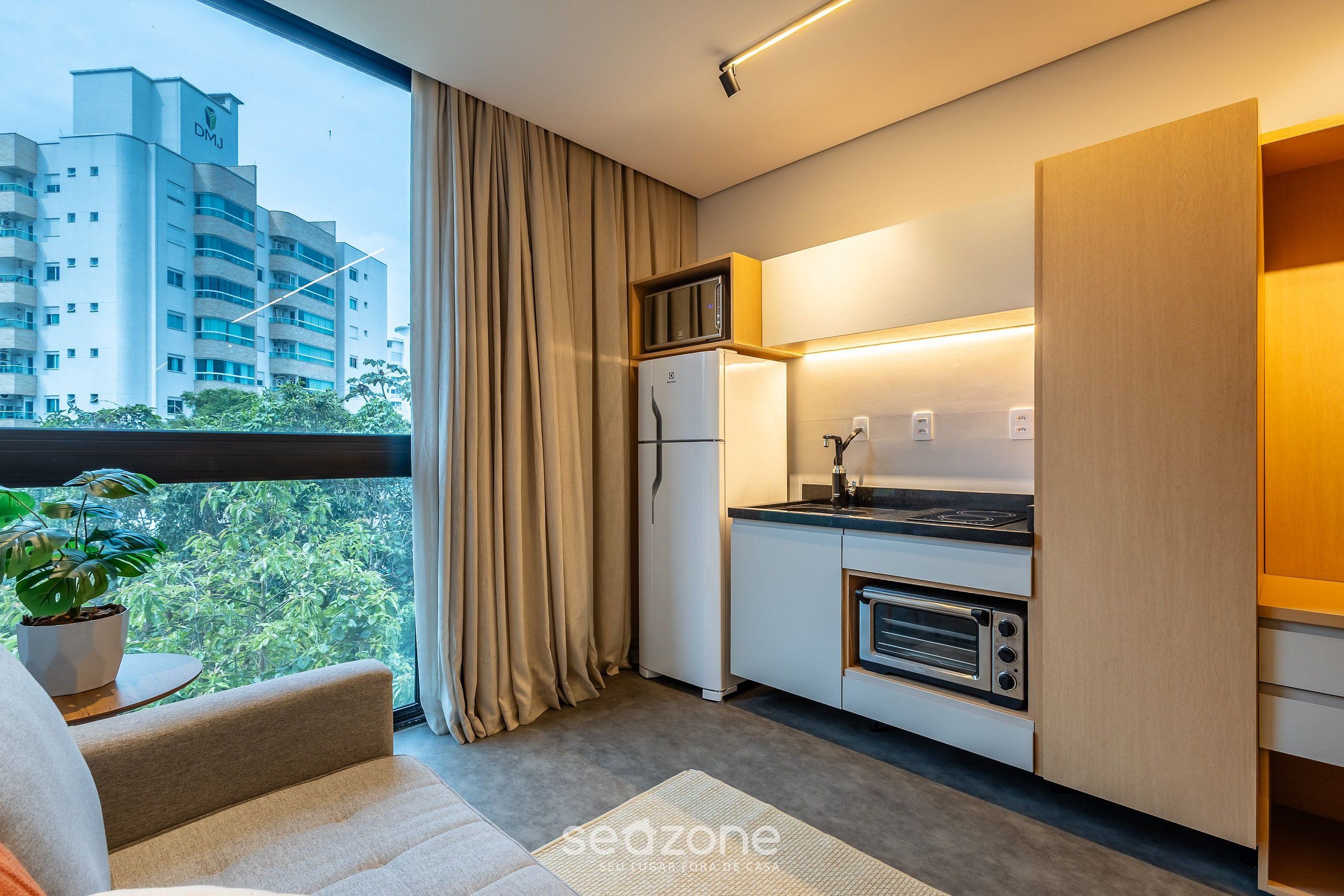 A modern kitchen with a built-in microwave, oven, and refrigerator. A large window with curtains offers a view of a cityscape.