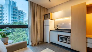 A modern kitchen with a built-in microwave, oven, and refrigerator. A large window with curtains offers a view of a cityscape.
