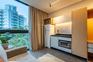 A modern kitchen with a built-in microwave, oven, and refrigerator. A large window with curtains offers a view of a cityscape.