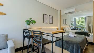 A hotel room with a bed, a desk with two chairs, a potted plant, and artwork on the wall.