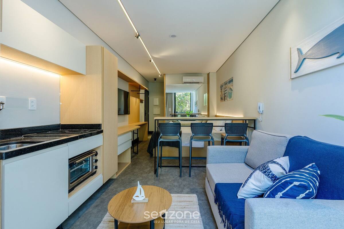 A modern kitchen with a built-in oven, a dining area with two chairs, and a sofa with decorative pillows.