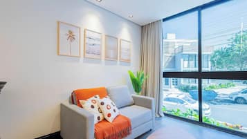 A modern room with a grey sofa, a large window, and framed artwork on the wall.