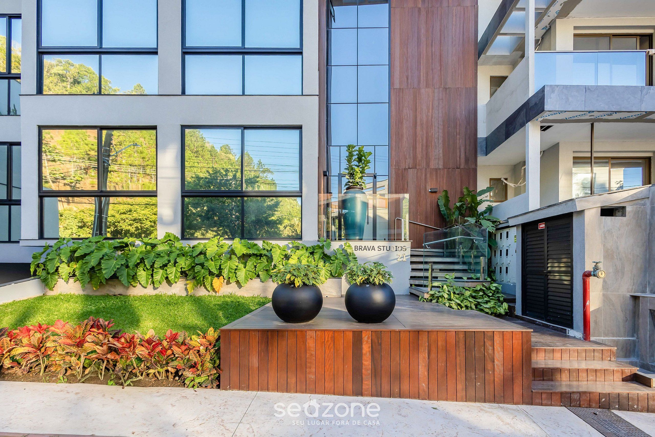 Un edificio moderno con amplios ventanales, una terraza de madera y un letrero que dice "BRAVA STUDIOS".