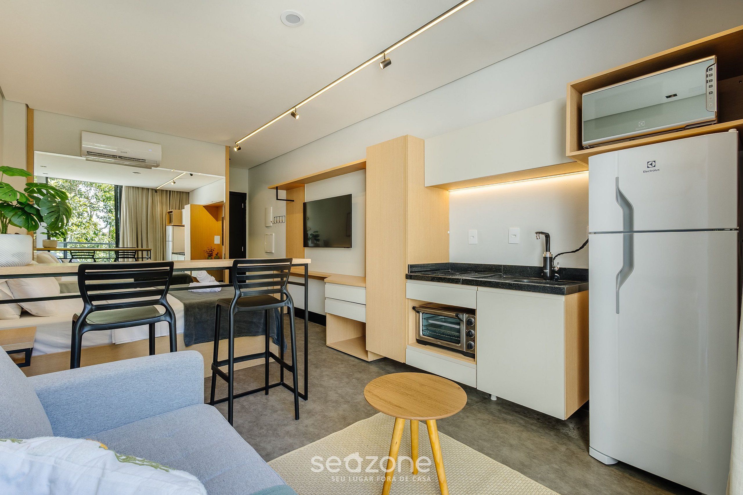 A compact kitchen with a built-in oven, a refrigerator, and a microwave. There is a dining area with a table and chairs, and a sofa in the foreground.