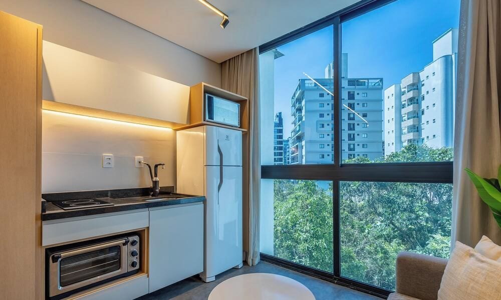 Cocina moderna con electrodomésticos integrados, un ventanal con vista a la ciudad y un taburete blanco redondo.