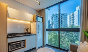 A modern kitchen with built-in appliances, a large window with a city view, and a round white stool. - Sua estadia próxima da Praia Brava - BSO (Balneário Camboriú)