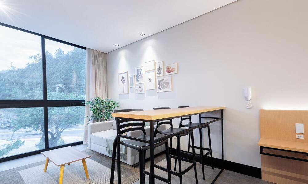 A modern room with a large window, a dining table with chairs, a sofa, and a small table.