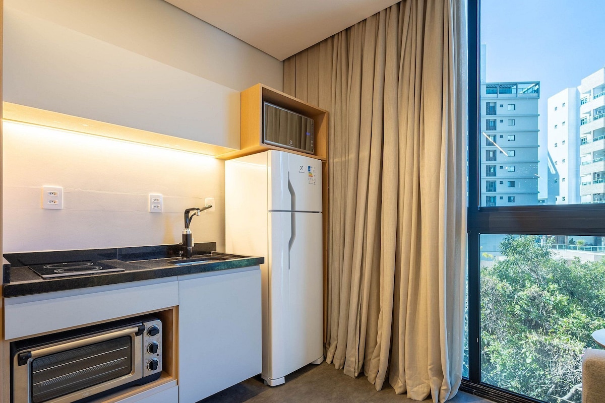 Una cocina compacta con horno empotrado, refrigerador y ventana con cortinas.
