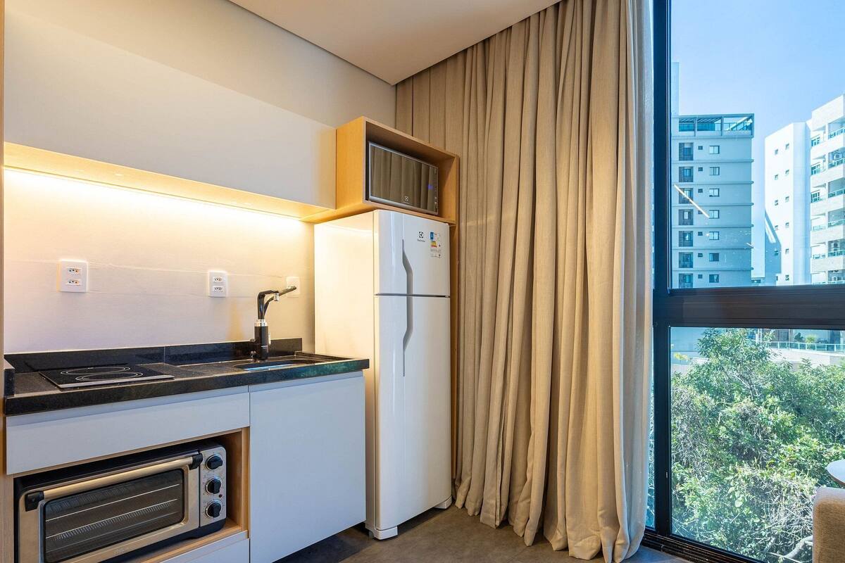 A compact kitchen with a built-in oven, a refrigerator, and a window with curtains.