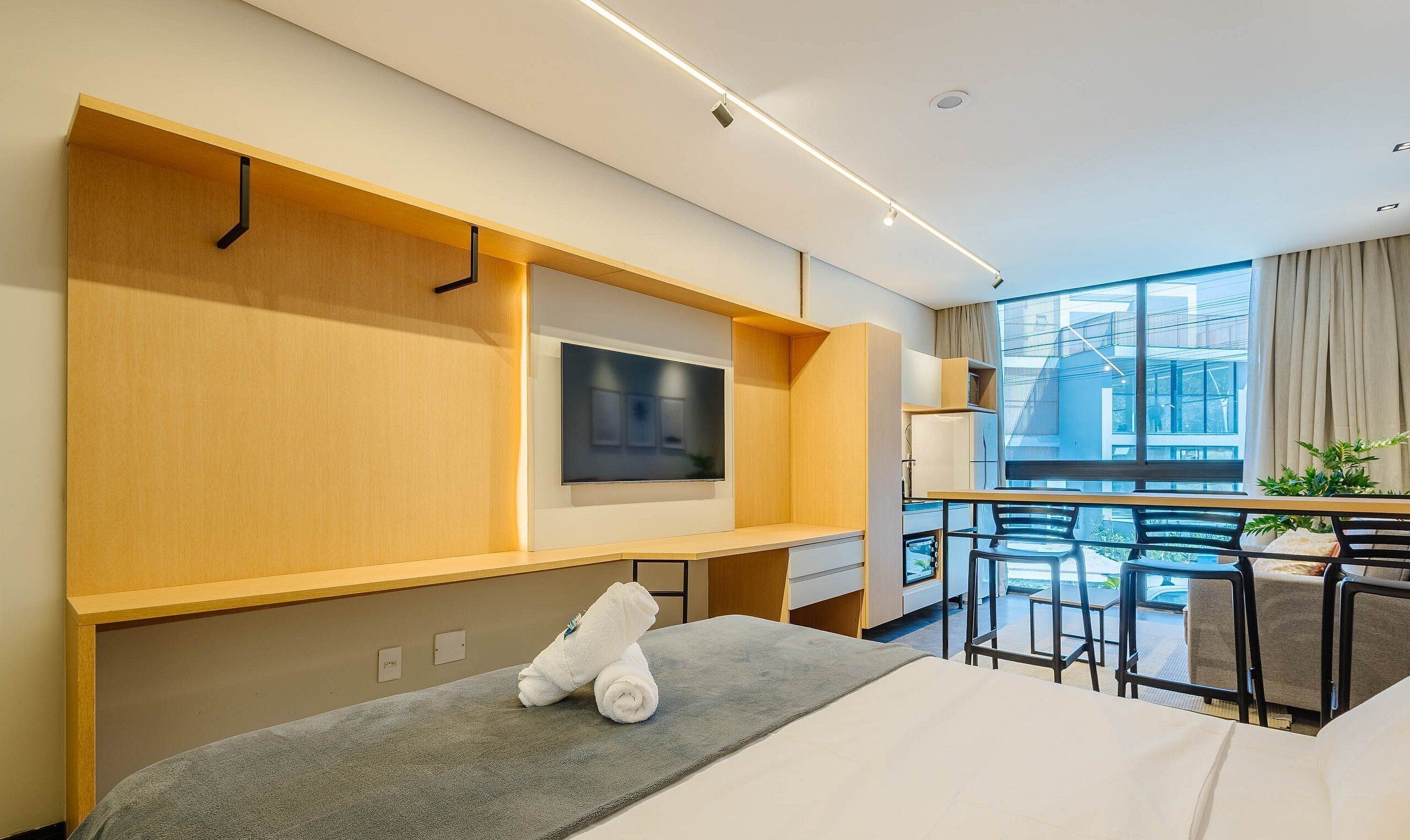 Ein modernes Hotelzimmer mit großem Fenster, Flachbildfernseher, kleinem Schreibtisch und einer gemütlichen Sitzecke.