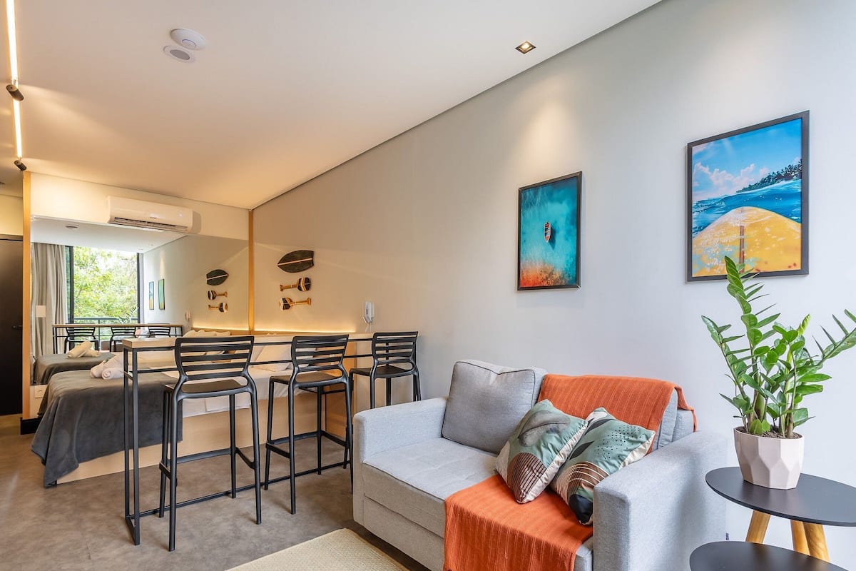 A modern living room with a grey sofa, a dining area with black chairs, and two paintings on the wall.