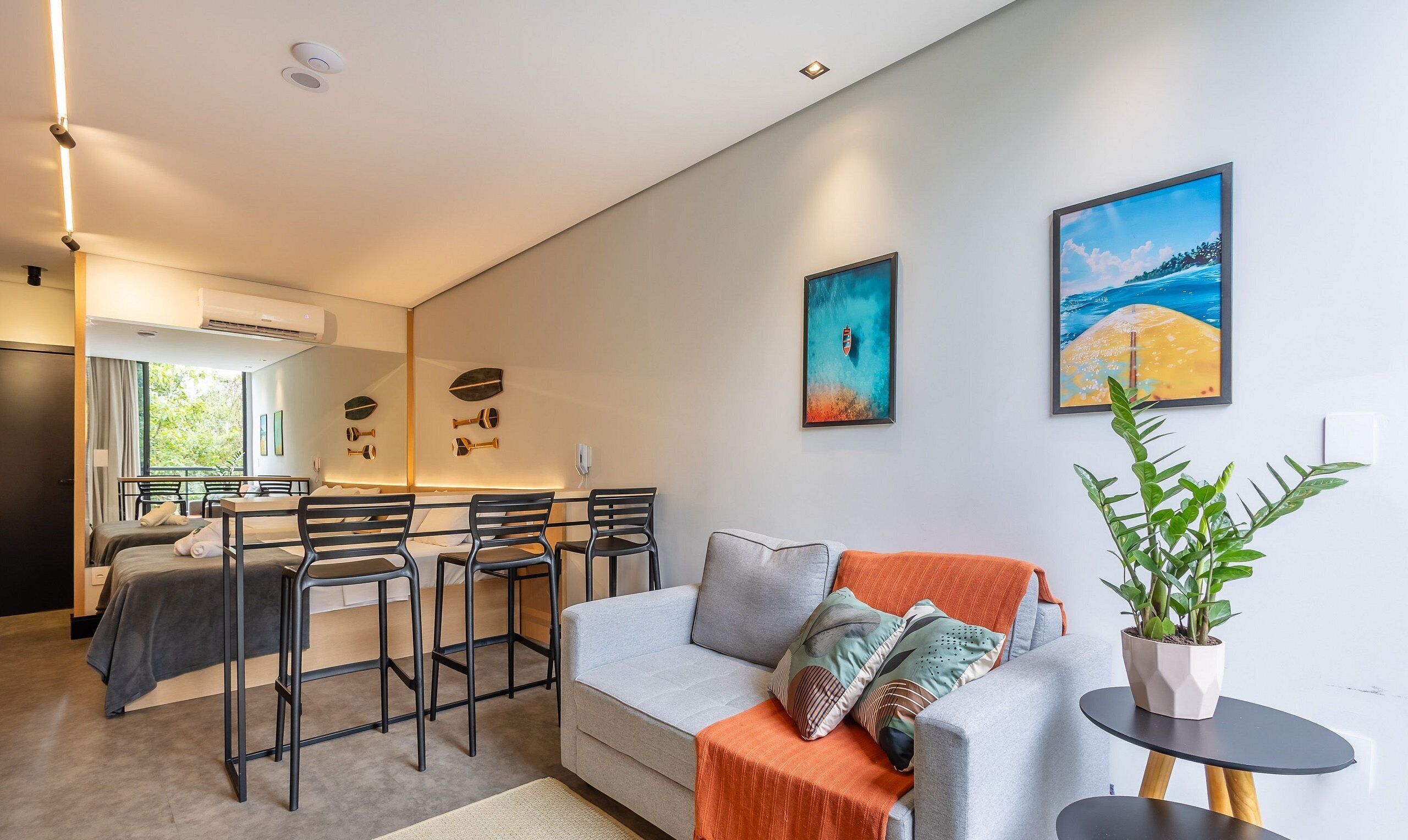 Ein modernes Wohnzimmer mit einem grauen Sofa, einem Essbereich mit schwarzen Stühlen und zwei Bildern an der Wand.