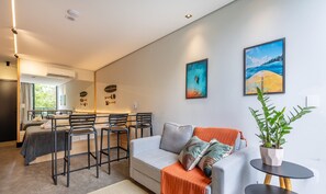 A modern living room with a grey sofa, a dining area with black chairs, and two paintings on the wall. - Sua estadia próxima da Praia Brava - BSO (Balneário Camboriú)