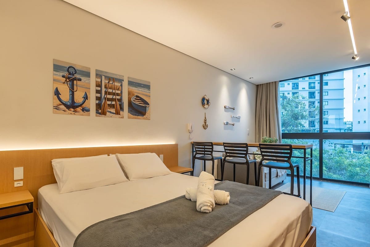 A modern hotel room with a large bed, a desk, and a balcony with chairs.
