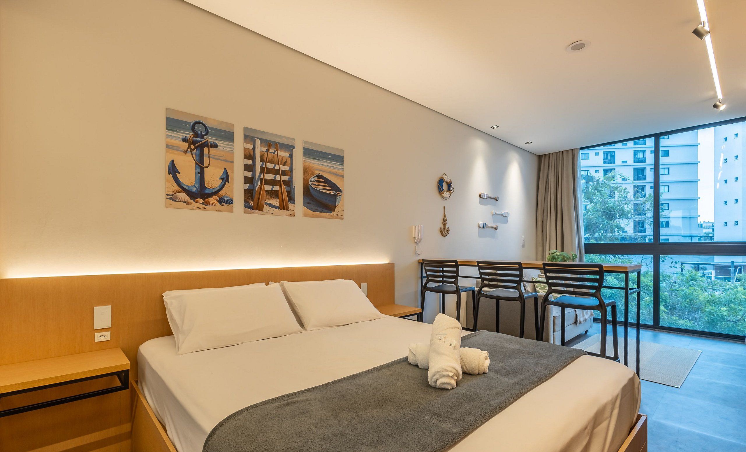 A modern hotel room with a large bed, a desk, and a balcony with chairs.