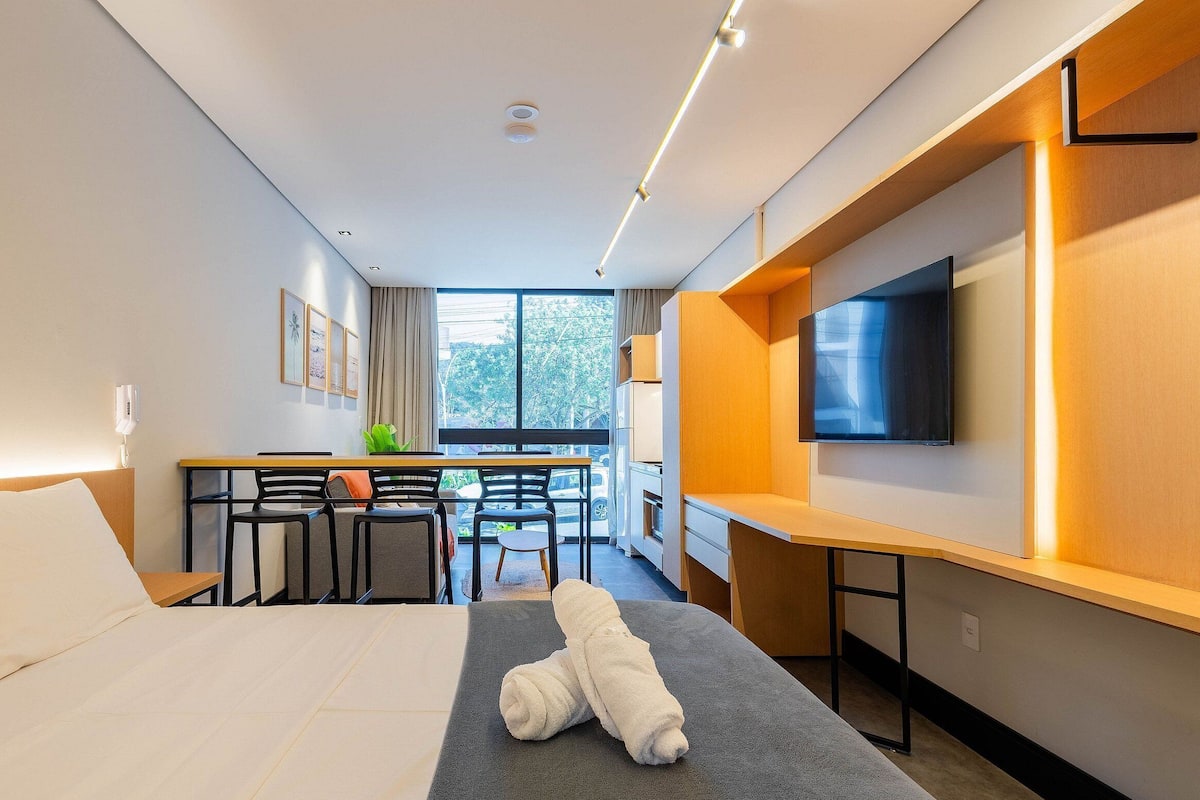 A hotel room with a bed, a desk with chairs, a TV, and a window with a view of the outside.
