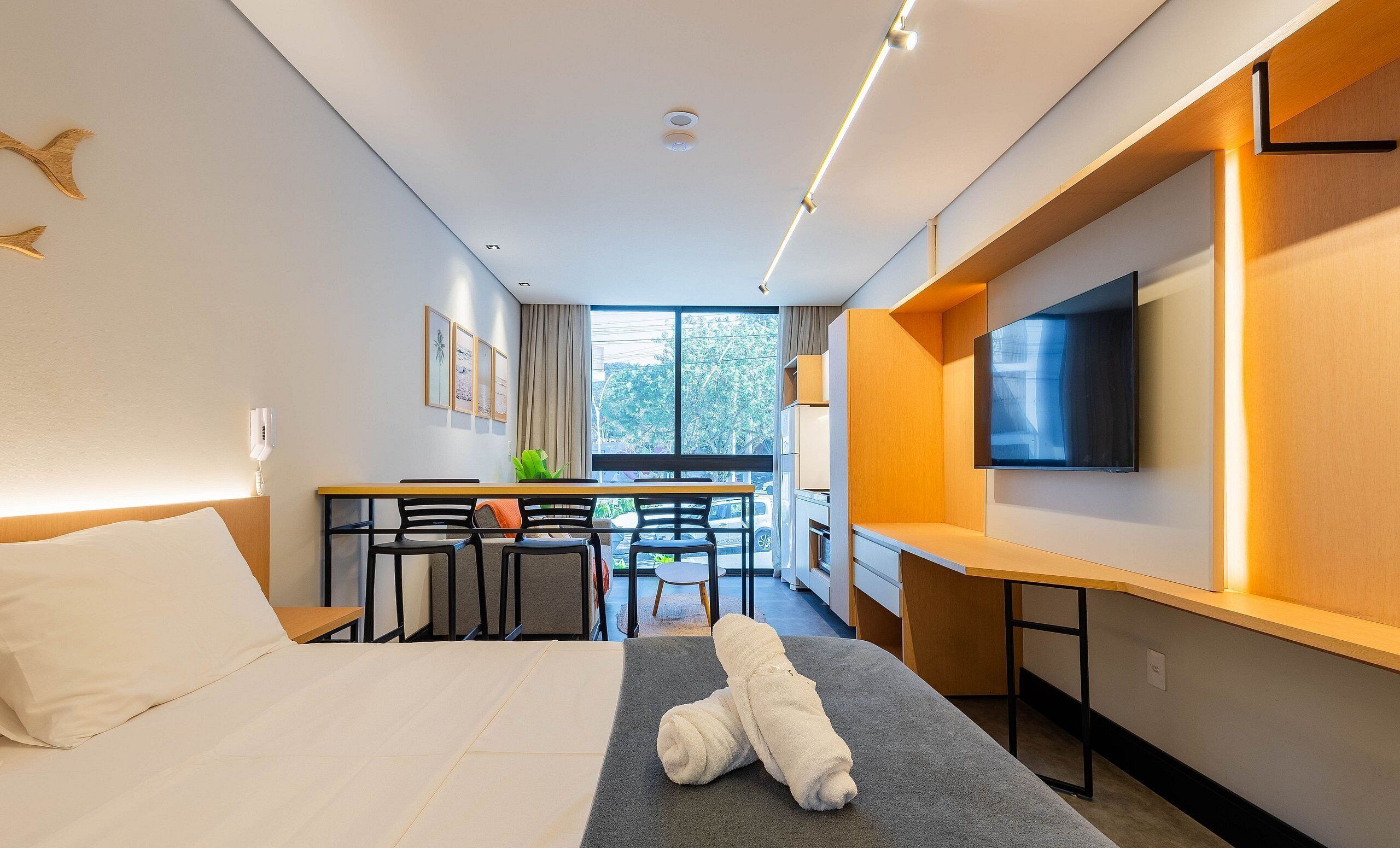 A hotel room with a bed, a desk with chairs, a TV, and a window with a view of the outside.
