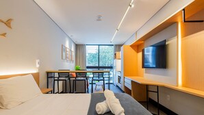 Una habitación de hotel con cama, escritorio con sillas, televisor y ventana con vistas al exterior.