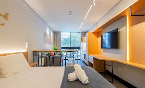 Una habitación de hotel con cama, escritorio con sillas, televisor y ventana con vistas al exterior.
