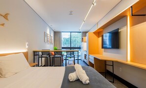 A hotel room with a bed, a desk with chairs, a TV, and a window with a view of the outside. - Sua estadia próxima da Praia Brava - BSO (Balneário Camboriú)
