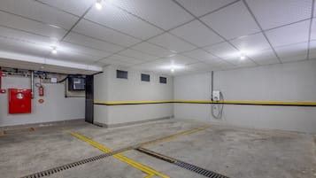 Een schone, goed verlichte parkeergarage met betonnen vloeren, gele veiligheidslijnen en een brandblusser aan de linkerkant.