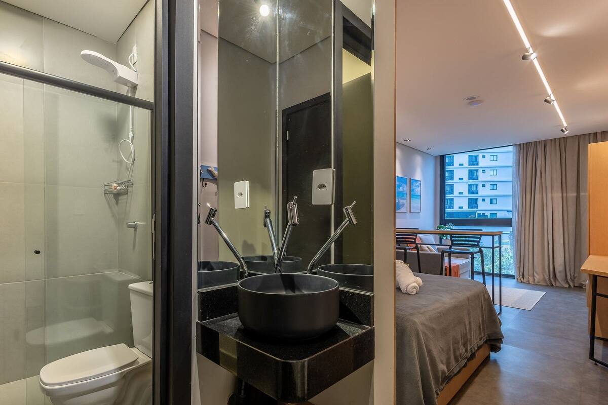 A modern bathroom with a glass shower enclosure, a black sink with a large basin, and a toilet.