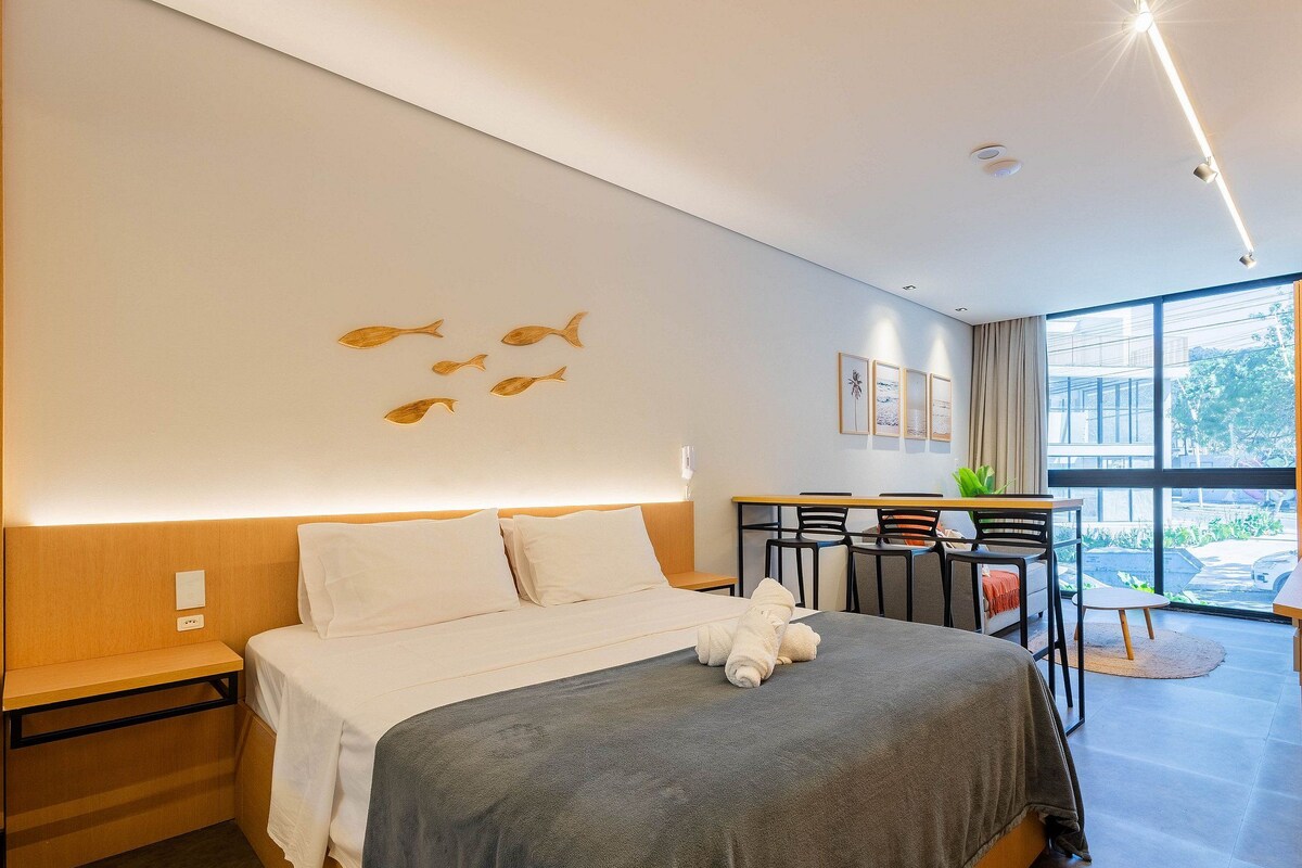 A modern hotel room with a bed, a desk, and a view of the outdoors.