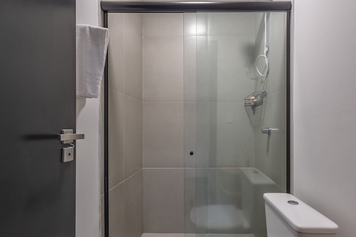 A modern bathroom with a glass shower enclosure, a toilet, and a towel hanging on the door.