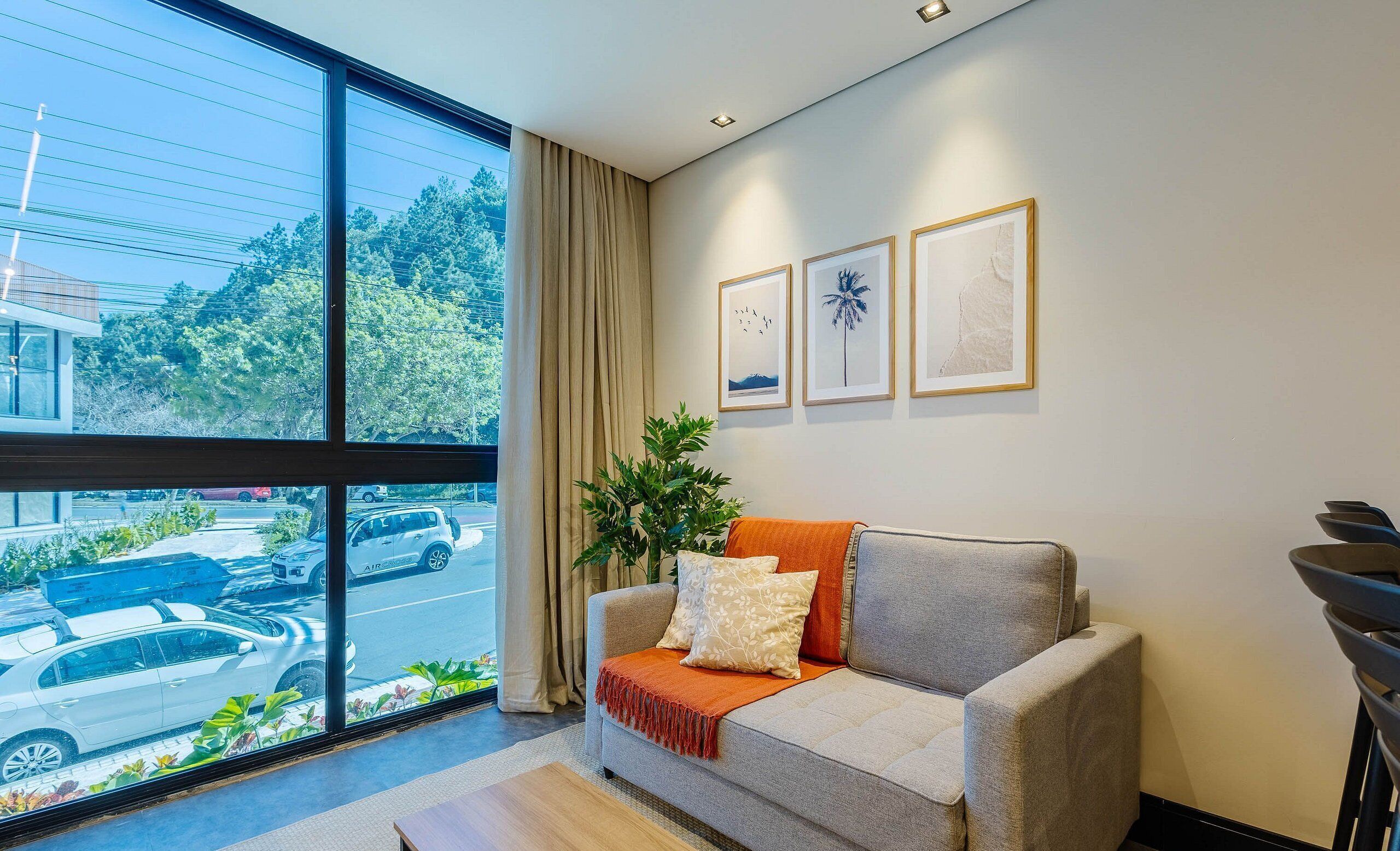 Ein modernes Wohnzimmer mit großem Fenster, einem grauen Sofa, einer Pflanze und gerahmten Kunstwerken an der Wand.
