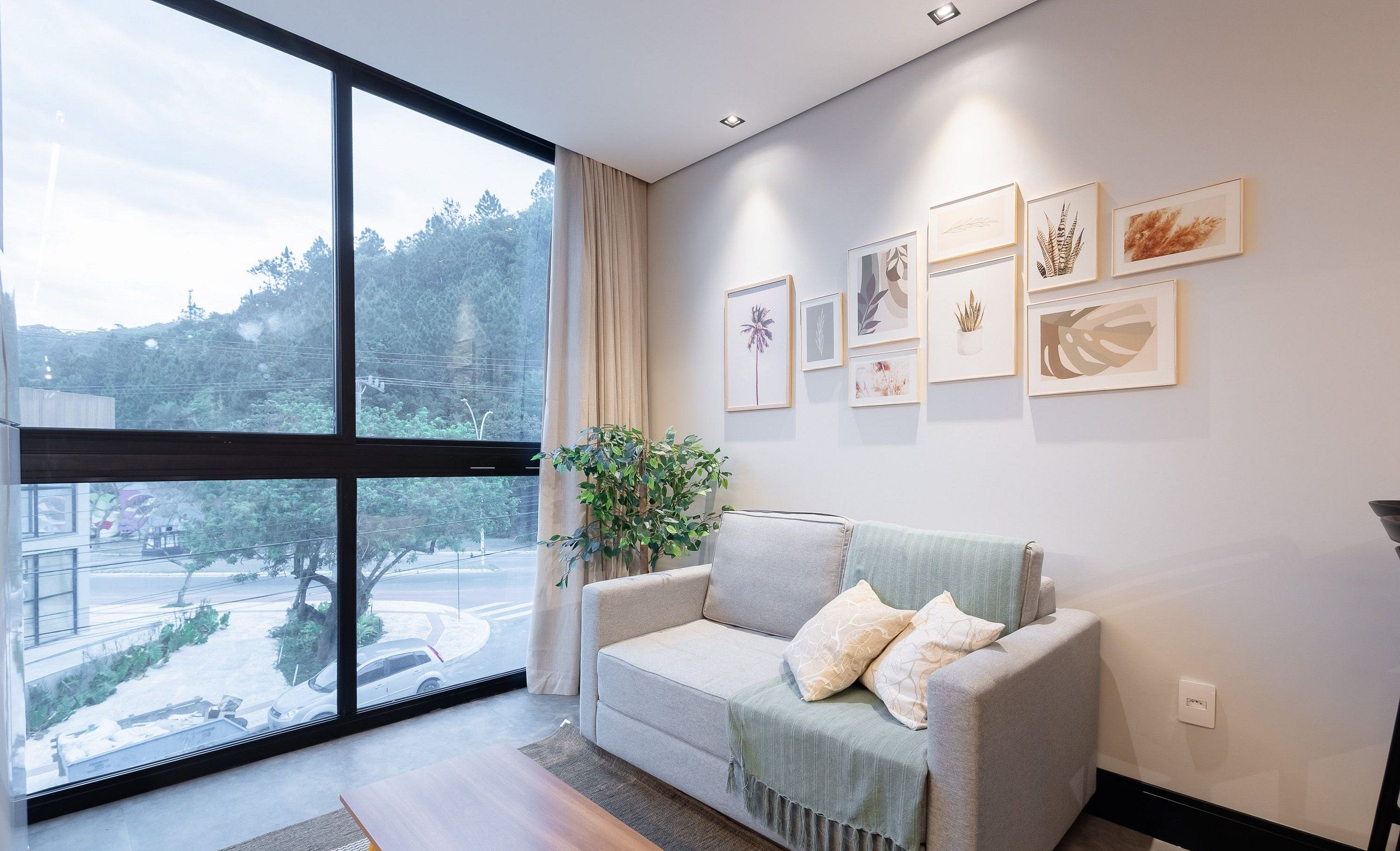 A modern living room with a large window, a grey sofa, and a potted plant.
