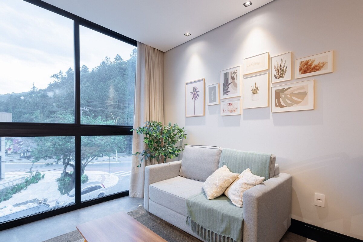 A modern living room with a large window, a grey sofa, and a potted plant.
