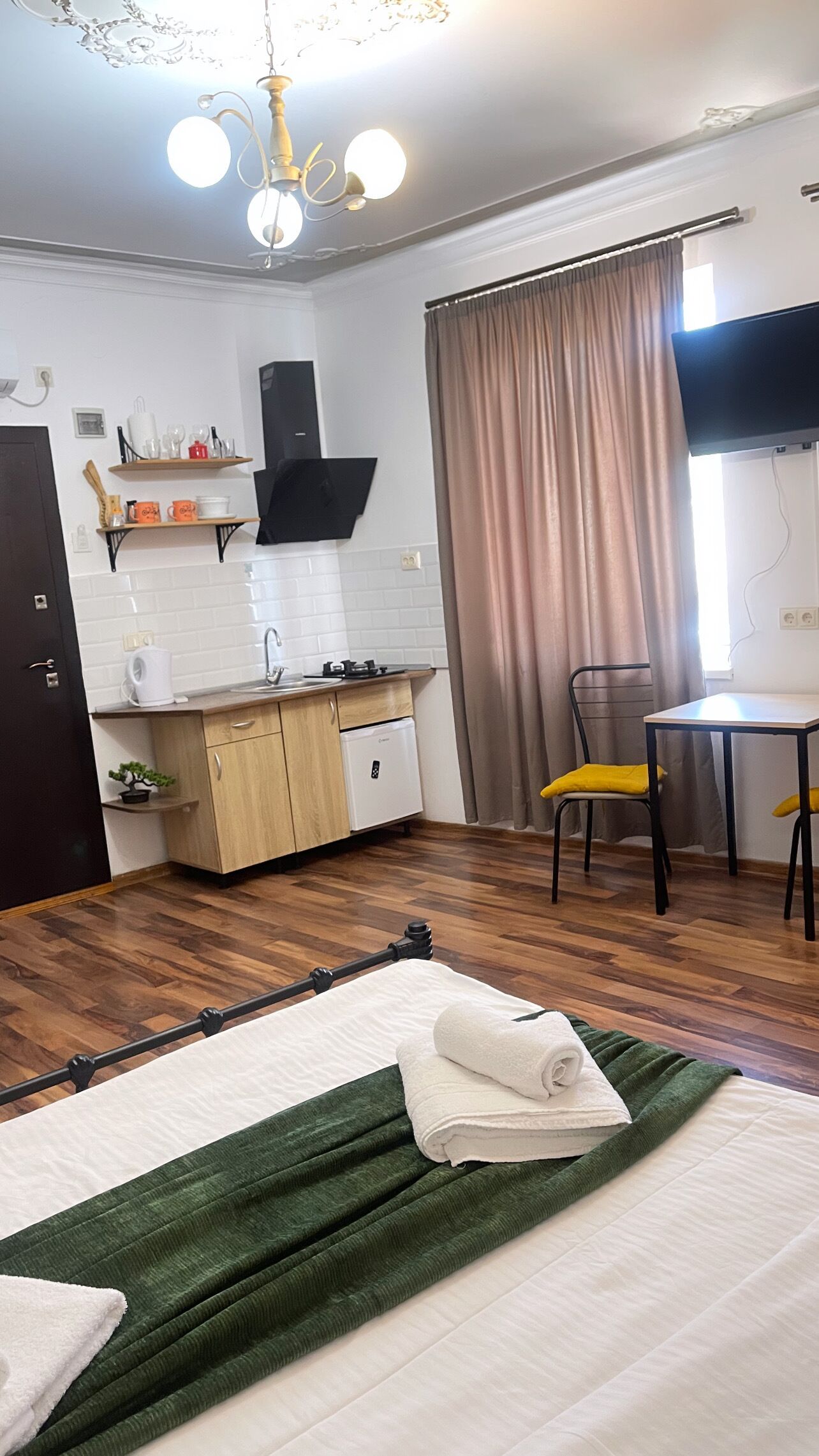 A compact room with a bed, a small kitchenette, a dining area, and a TV.