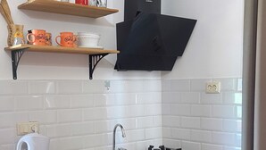 A compact kitchen with wooden cabinets, a white dishwasher, a gas stove, and a black range hood. - Warm House (Tbilisi)