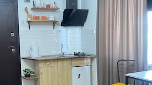 A compact kitchen with wooden cabinets, a built-in stove, and a small dining area with a chair. - Warm House (Tbilisi)