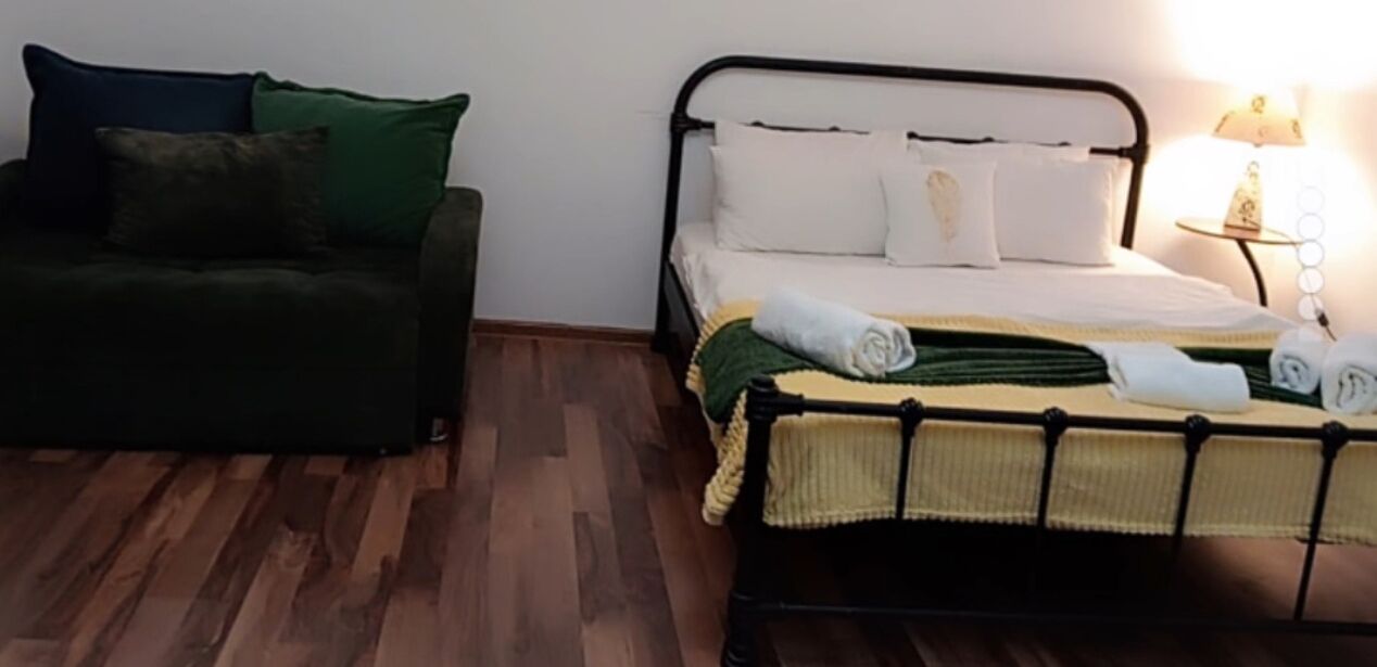 A room with a bed, a green sofa, and a nightstand with a lamp.