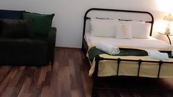 A room with a bed, a green sofa, and a nightstand with a lamp.