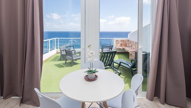 A balcony with a view of the ocean, a round table with chairs, and a potted orchid. - PentHouse Loft - Terrace & Natural Pool (Gáldar)