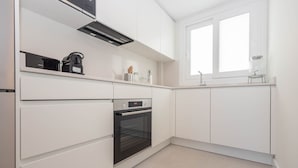 Una cucina moderna con mobili bianchi, forno integrato, macchina da caffè e una finestra che fa entrare luce naturale.