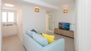 Un soggiorno moderno con un divano blu chiaro, una TV a schermo piatto e due applique a parete.
