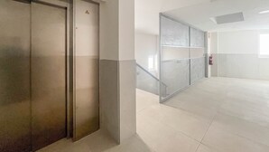 Un corridoio con un ascensore chiuso, una parete divisoria in vetro e un estintore al muro.