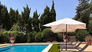A swimming pool with a green artificial turf edge, surrounded by lounge chairs and an umbrella.