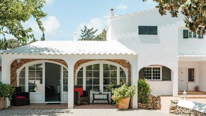 A white building with a covered patio area featuring a stone archway, a seating area with a table, and potted plants.