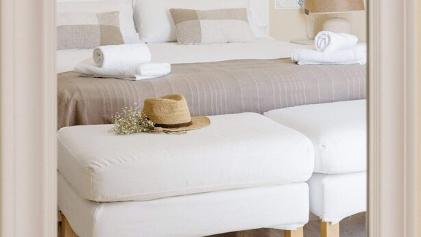 A bedroom with a bed, two white upholstered benches, a lamp, and a mirror.