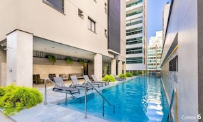 A modern building with a swimming pool, lounge chairs, and a covered seating area. - IFT - Ed. Infinity Tower Flat 350m From Meia Praia (Itapema)