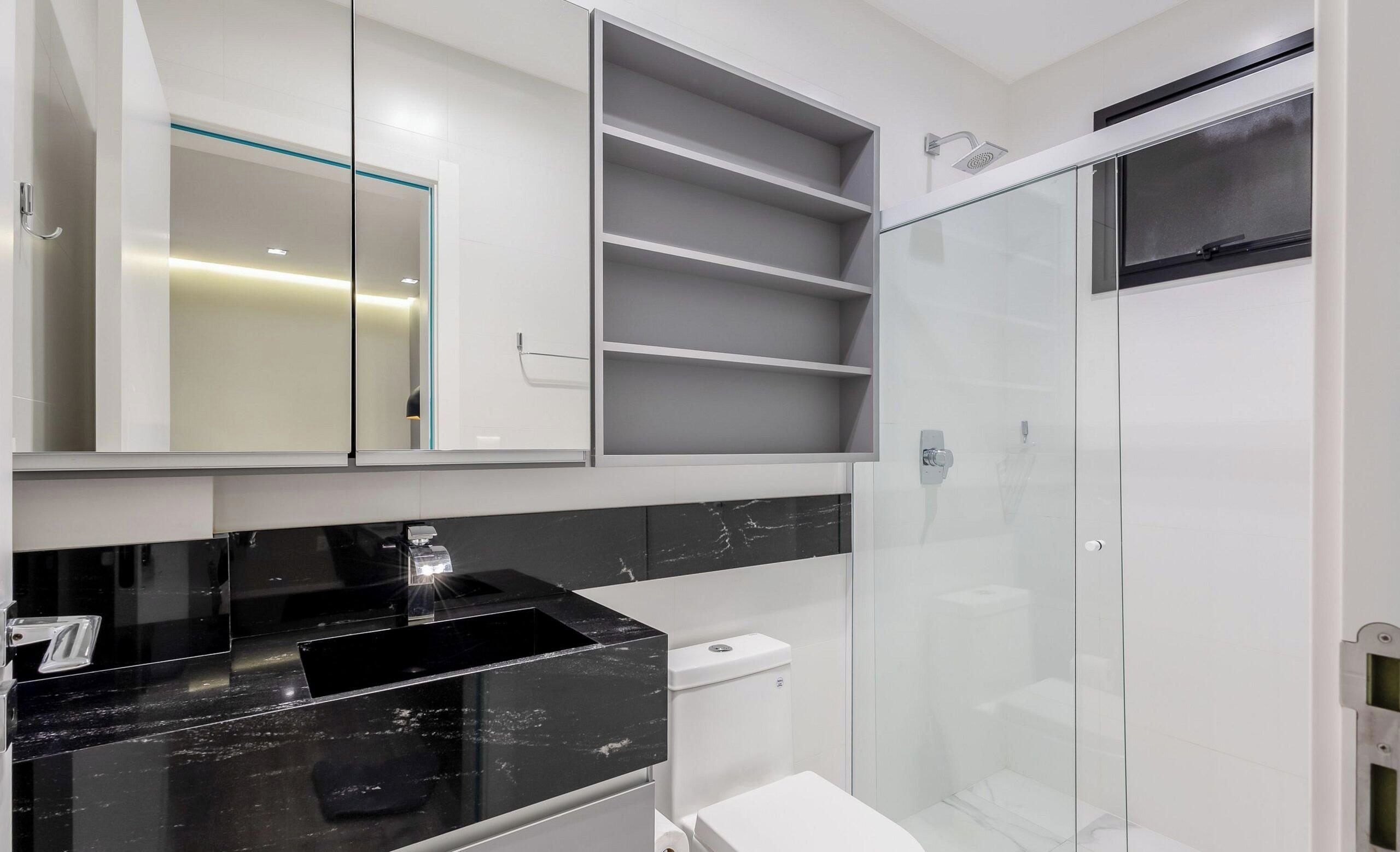 Un baño moderno con lavamanos de mármol negro, inodoro, cabina de ducha de vidrio y estantes empotrados.