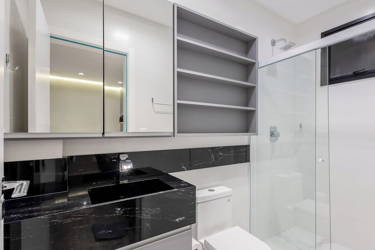 A modern bathroom with a black marble sink, a toilet, a glass shower enclosure, and built-in shelves.