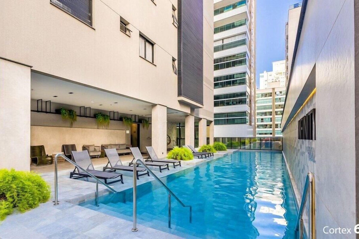 A modern building with a swimming pool, lounge chairs, and a covered seating area.