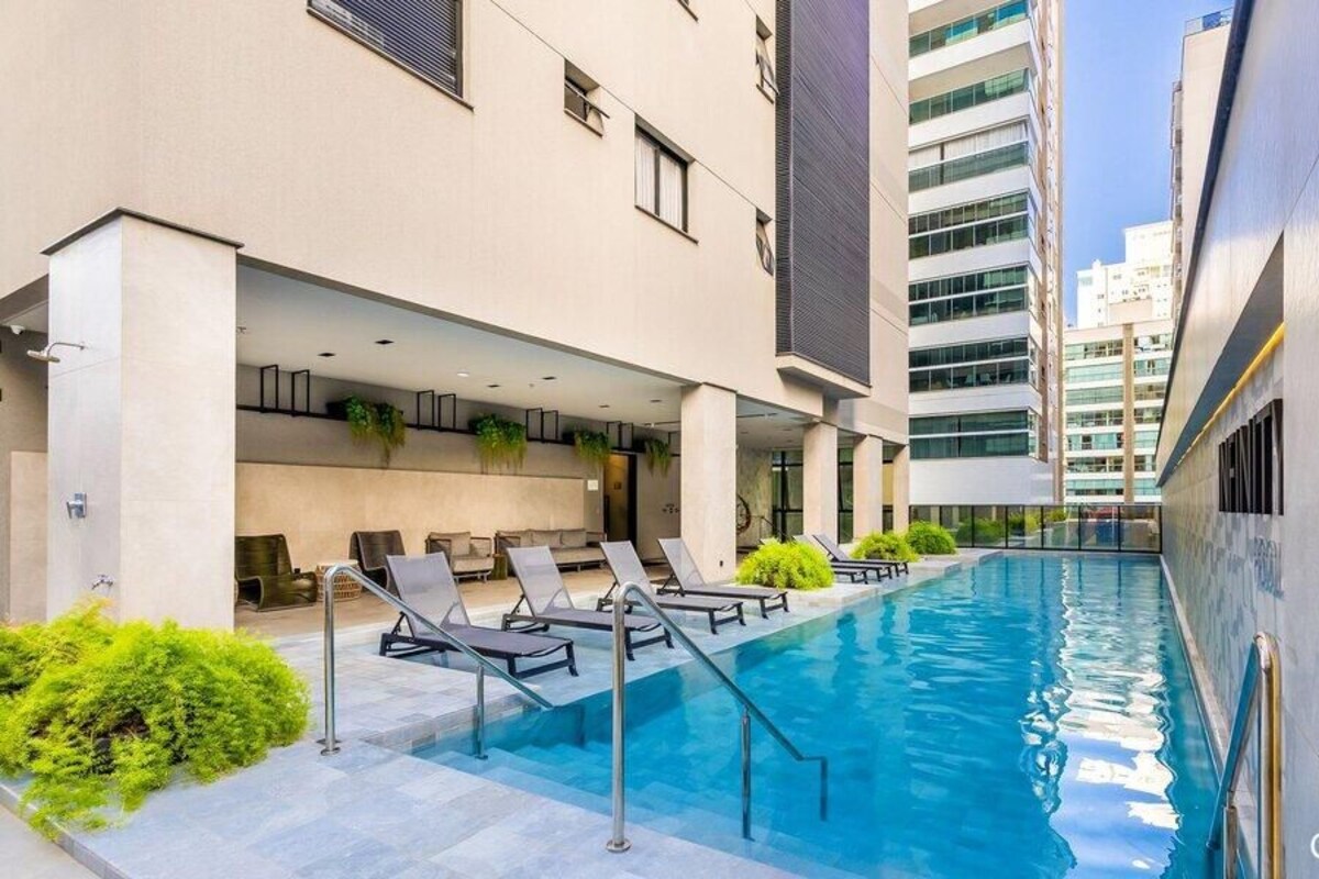 A modern building with a swimming pool, lounge chairs, and a covered seating area.