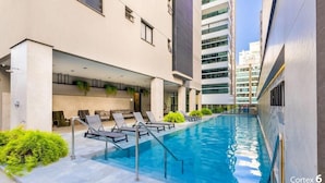 A modern building with a swimming pool, lounge chairs, and a covered seating area. - IFT - Ed. Infinity Tower Flat 350m From Meia Praia (Itapema)